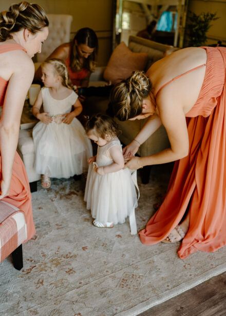 A bridesmaid ties a bow on the back of a flower girl's dress.