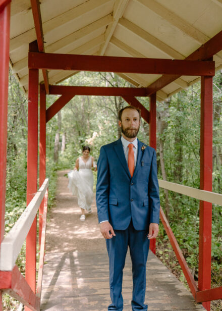 Anna walks up behind Jason for their first look on a red covered bridge.