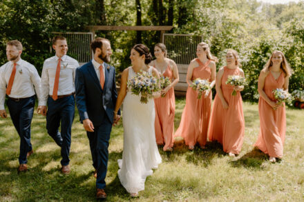 The wedding party walks through the orchard, smiling and laughing with one another.