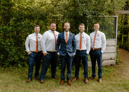 The groom poses with his groomsmen, smiling in a line.