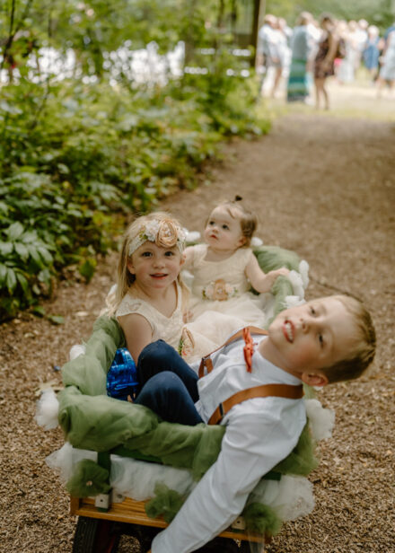 The flower girls and ring bearer sit in a wagon together after the ceremony.