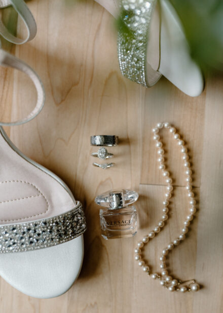 A close up of the wedding rings, rhinestone covered shoes, Versace perfume, and string of pearls.
