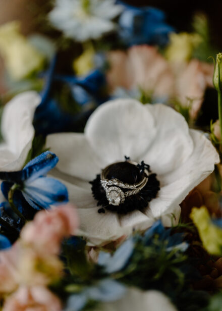 The bride's wedding and engagement rings rest atop a white flower.