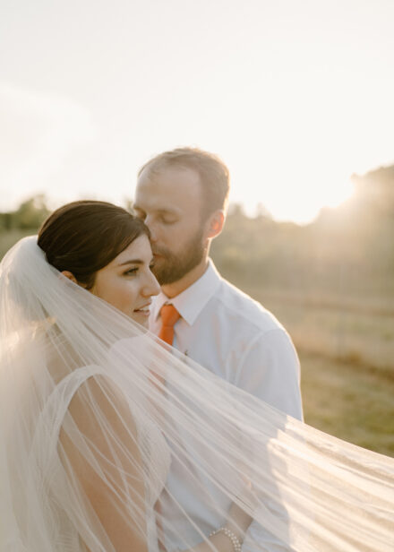 Anna's veil sweeps to the right side of the frame has Jason kisses the side of her head.