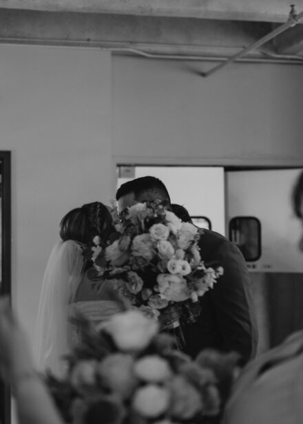 A candid photo of Connie and Taysir sharing a kiss, their faces covered by Connie's bouquet.