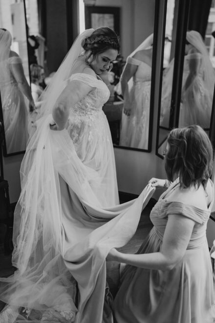 The bride's sister bustles her dress in front of a trifold mirror.