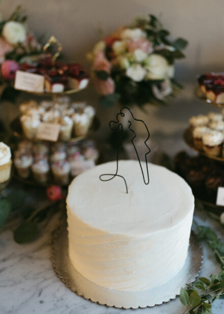A small, white wedding cake with a wire topper of a couple kissing.