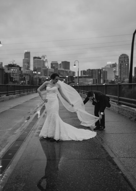 Matt sweeps Beth's veil out behind her on the stone arch bridge.