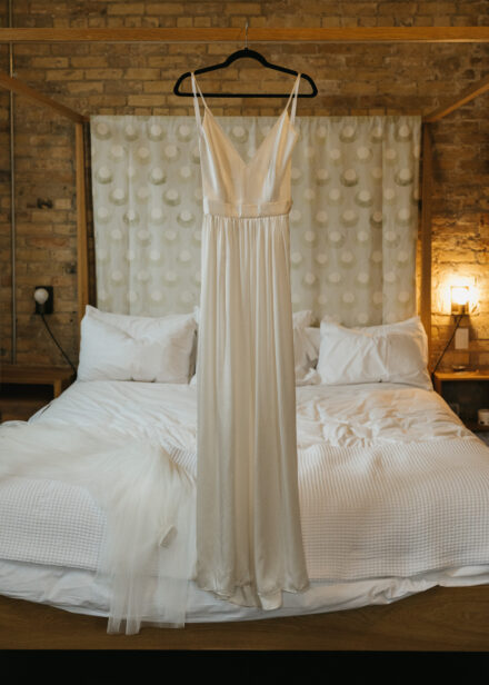 Beth's silky second dress hangs on the frame of the bed in Hotel Alma.