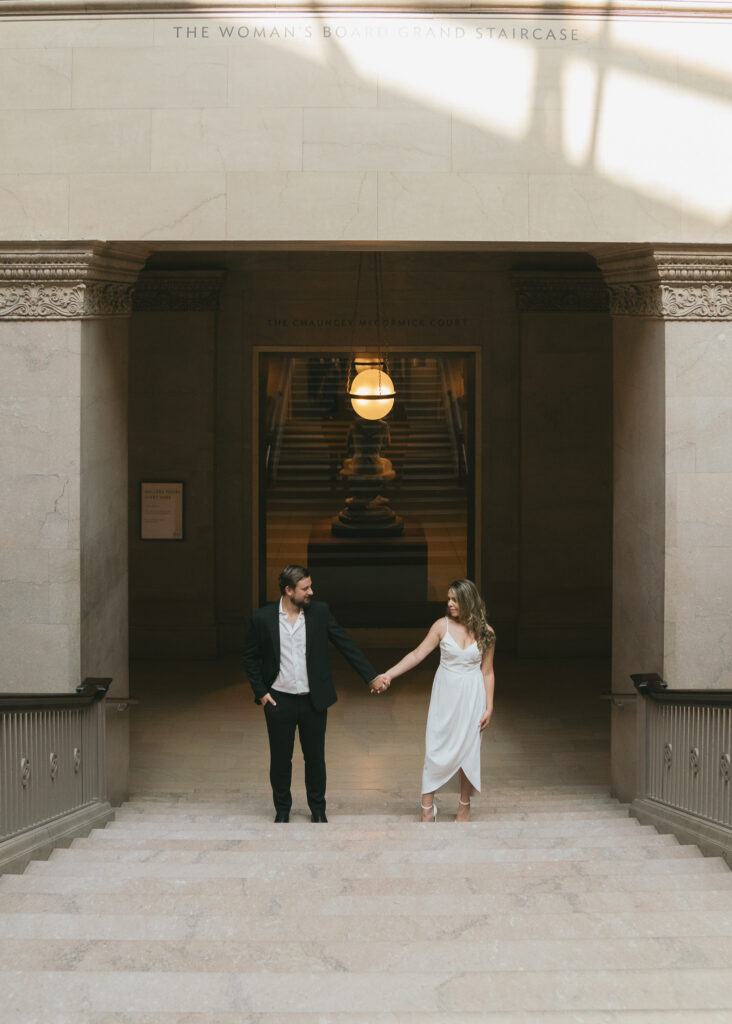 The couple holds hands at the bottom of the Grand Staircase.