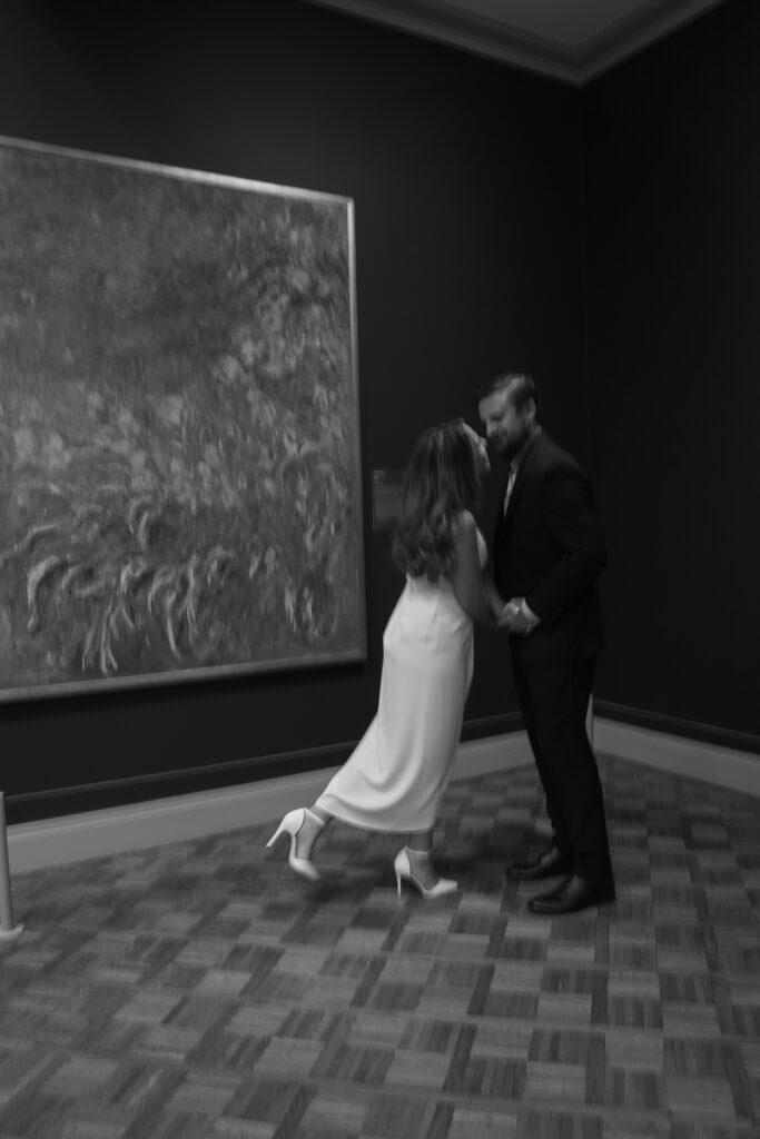 A blurry black and white image of a couple spinning in front of a painting.