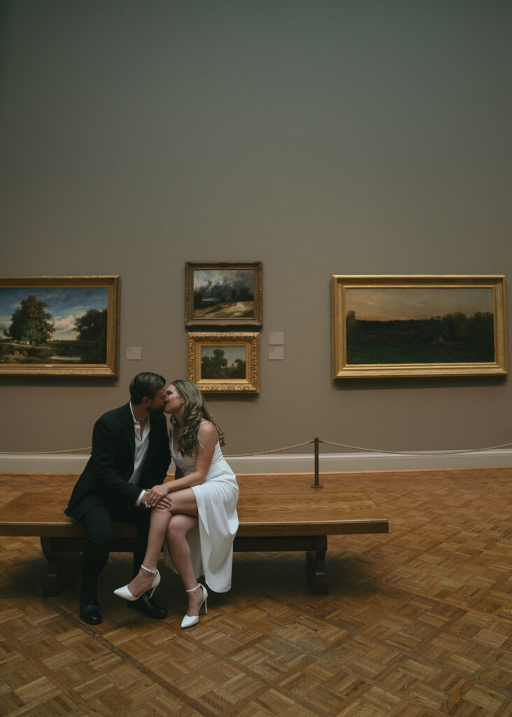 The couple sits on a bench in front of a gallery of paintings at the Art Institute of Chicago.