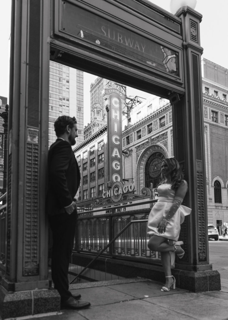 The couple leans against the entrance to the L, the Chicago Theater sign visible in the middle.