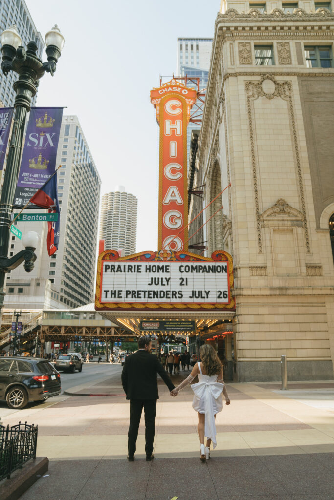 The couple holds hands in front of the Chicago Theater.