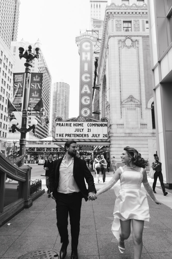 The couple runs down the sidewalk toward the camera, the Chicago Theater in the background.