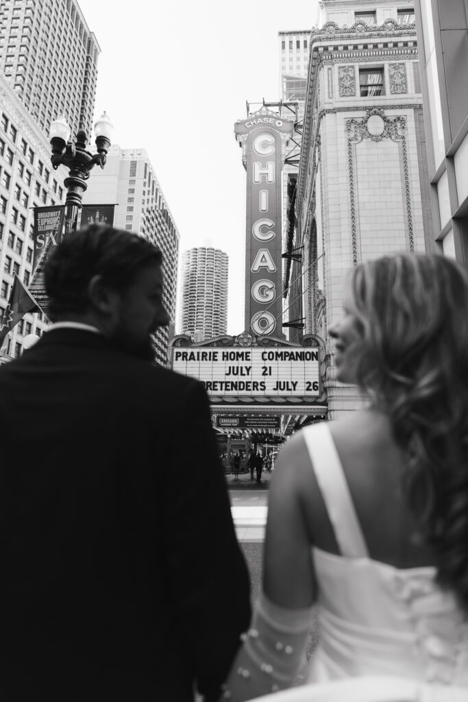 The couple smiles at each other, the Chicago Theater sign visible between them.