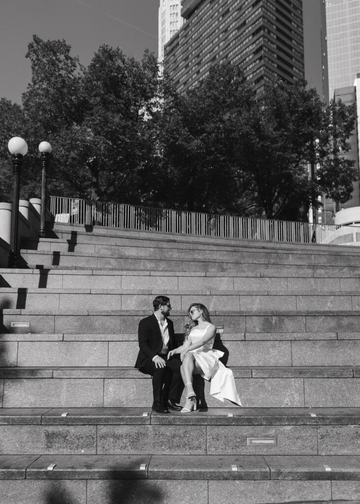 A black and white image of the couple sitting on a large staircase by the Chicago Riverwalk.