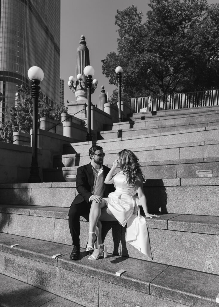 A black and white image of the couple sitting on a large staircase by the Chicago Riverwalk.