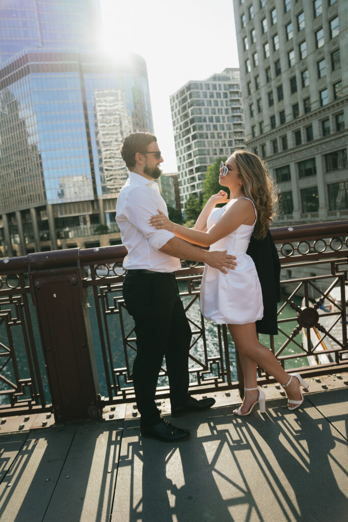 The couple stands in front of the Chicago River, the woman holding the man's jacket over her shoulder.