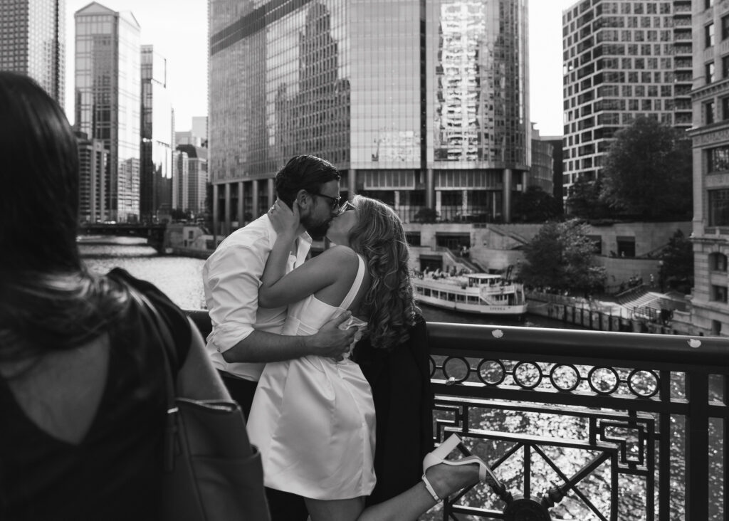 A couple kisses on a bridge overlooking the Chicago River, photo taken over the shoulder of a passerby.