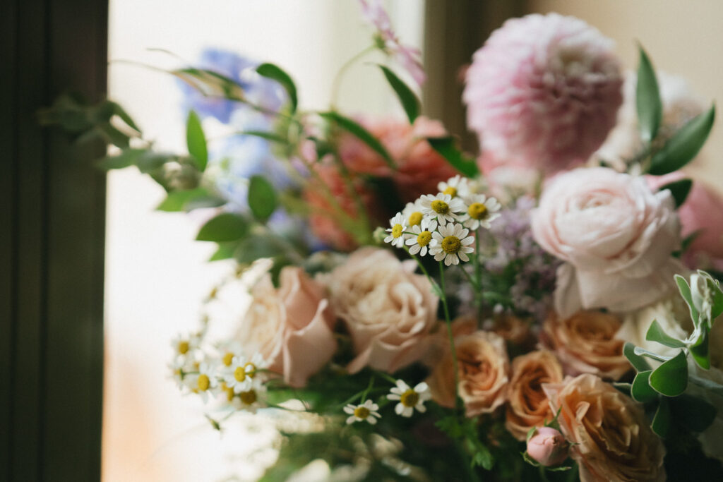 A close up of the bride's bouquet with daisies, dahlias, roses, and greenery.