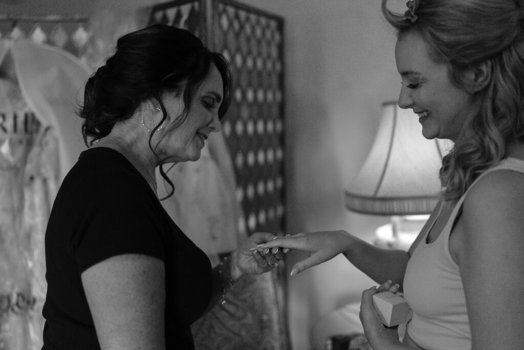 The bride with her hair in curlers smiles as she shows off her wedding ring to her mother.