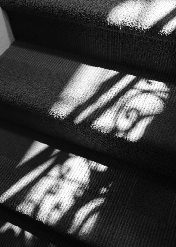 The sun shines on the stairs, shadows being thrown from the spirals on the wrought iron railing.