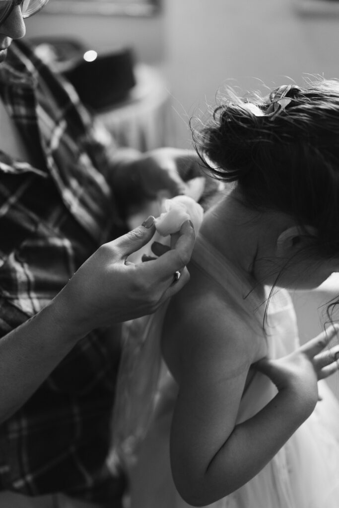 The bride's sister helps a flower girl tie a bow on the neck of her dress.