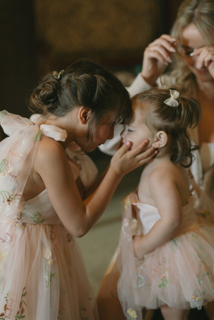 The flower girls giggle and press their faces together.