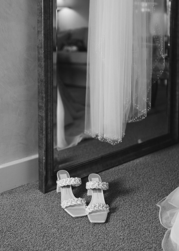 The bride's shoes sit underneath her veil hanging from a floor length mirror.