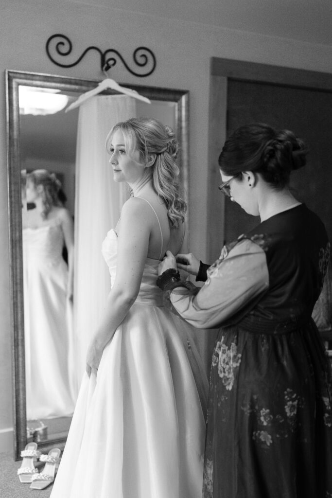 The bride's sister helps her button up the back of her dress.