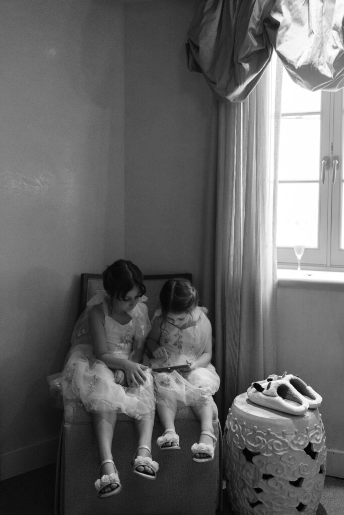 The two flower girls sit on a chair and read a book together.