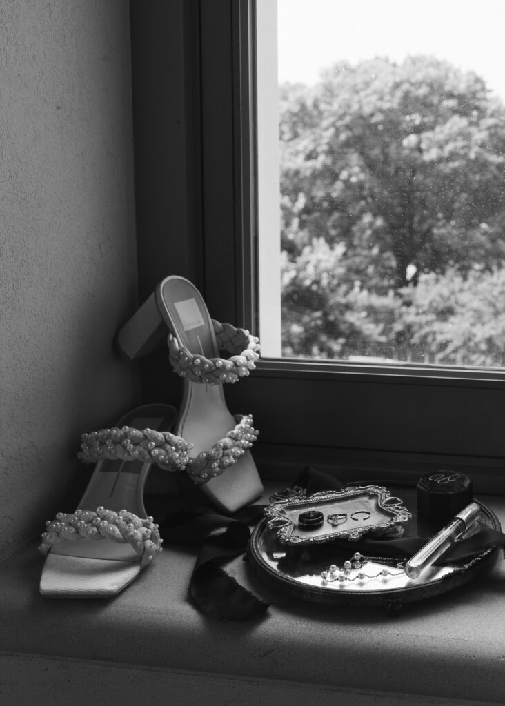 A bride's shoes, rings, and wedding details on a windowsill. 