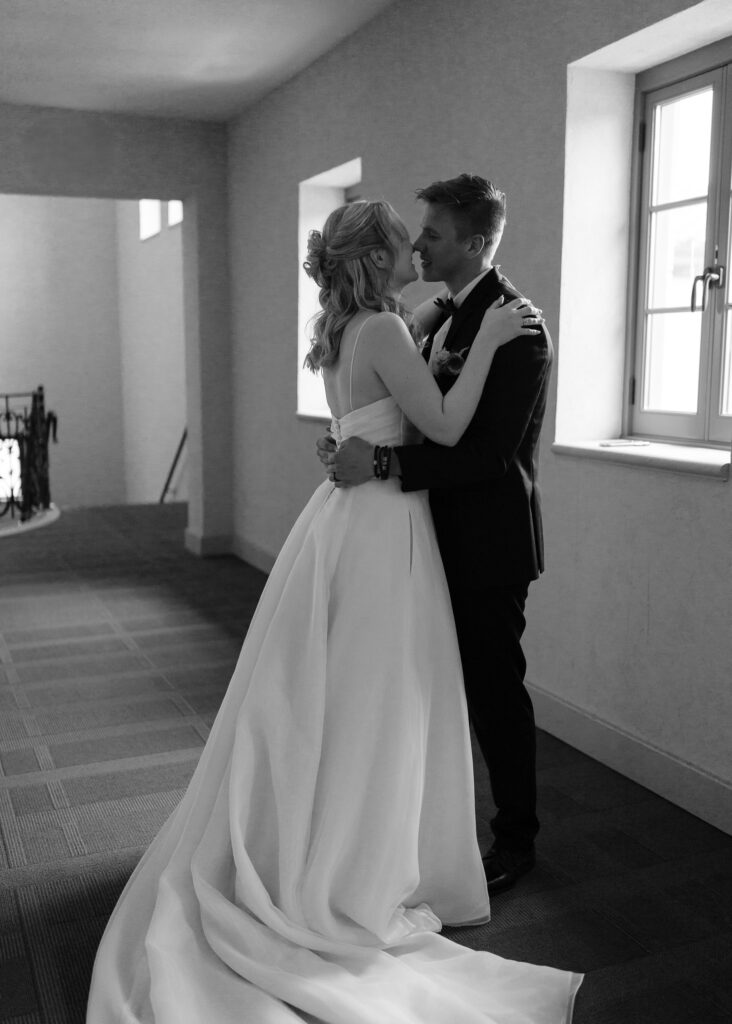 The couple leans in for a kiss on front of a window during their first look.