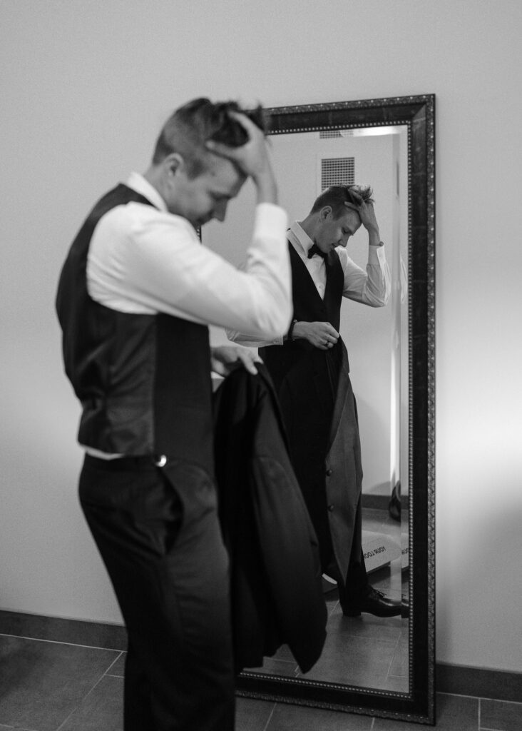 The groom stands in front of a mirror and fixes his hair.