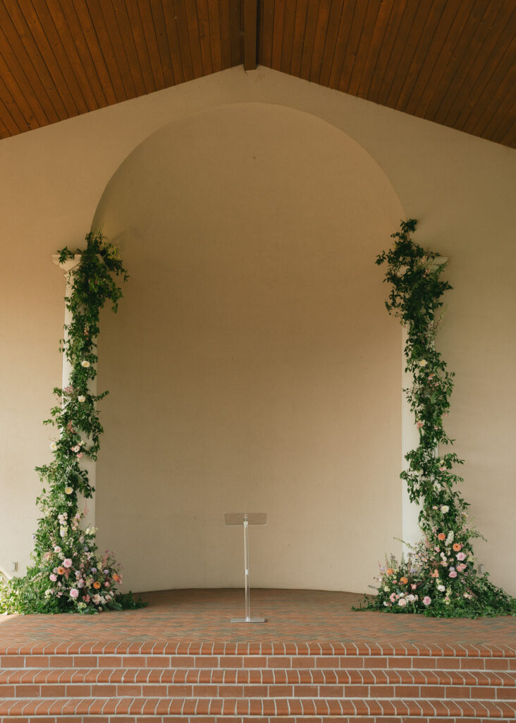 The archway at the back of the vineyard pavilion, flowers and greenery arching up toward the ceiling.