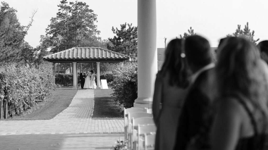 The bride walks down the aisle with both her parents as guests look back at them.