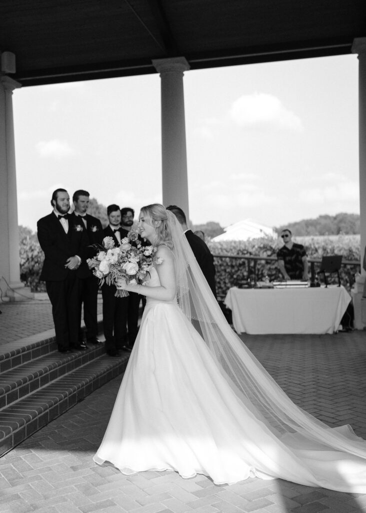 The bride and groom walk toward the dais of the pavilion, the bottom of the bride's dress illuminated in the sunlight.