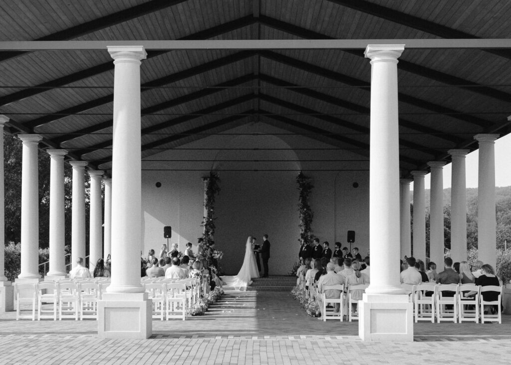 A black and white image of the wedding ceremony from the back of the pavilion.