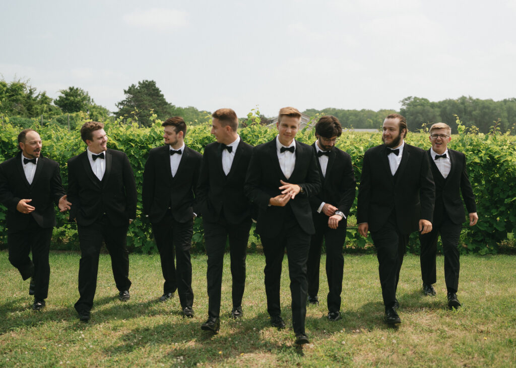 The groom and his groomsmen walking toward the camera in a vineyard.