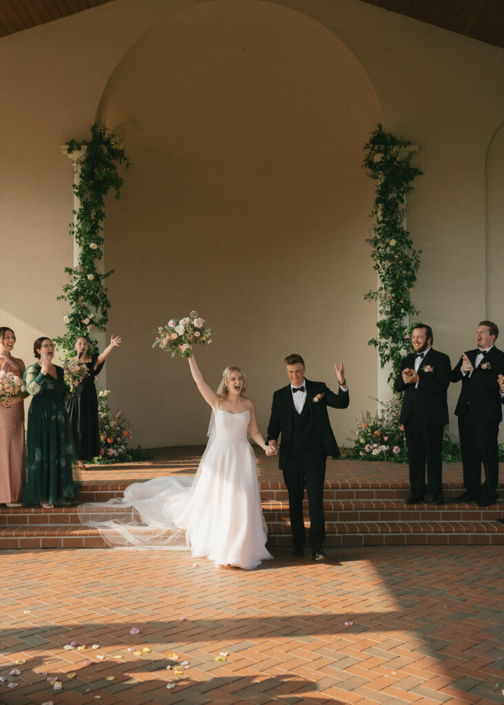 The couple throws their arms in the air in celebration as they walk back down the aisle after their ceremony.