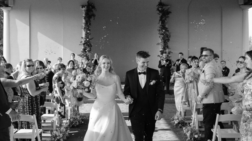 A black and white image of the couple walking back down the aisle as guests throw flower petals at them.