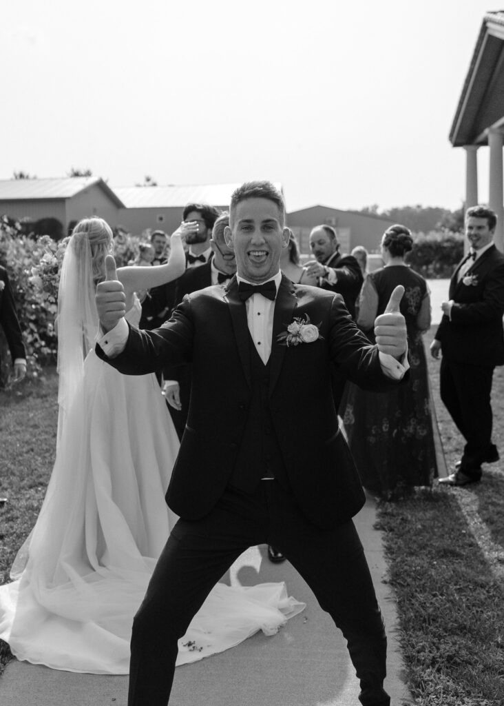 A groomsman sticks out his tongue at the camera and gives two thumbs up.