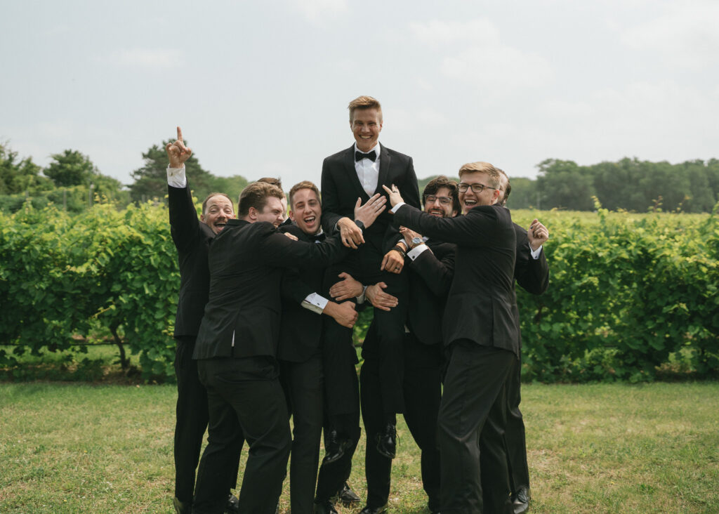 The groomsmen pick up the groom and set him on their shoulders as they cheer.