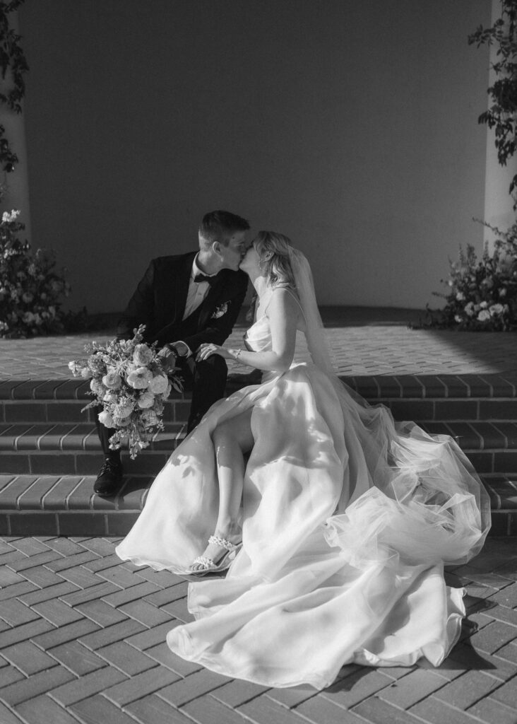 The couple kisses as they sit on the brick steps of the pavilion.