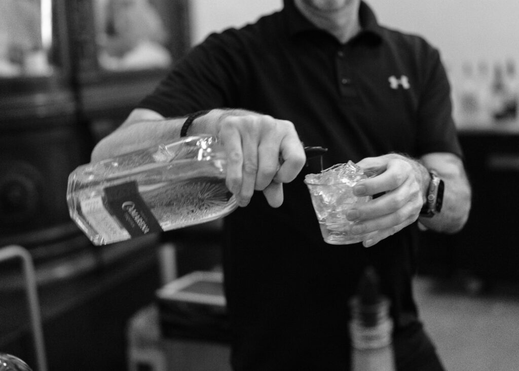 A slightly blurred close up of a bartender pouring vodka into an ice-filled glass.