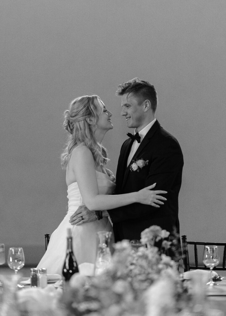 The couple wraps their arms around one another and smiles during their wedding reception.