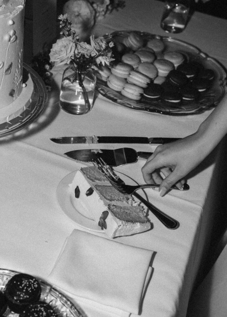 A close up of the bride's hand holding a fork next to a slice of wedding cake.