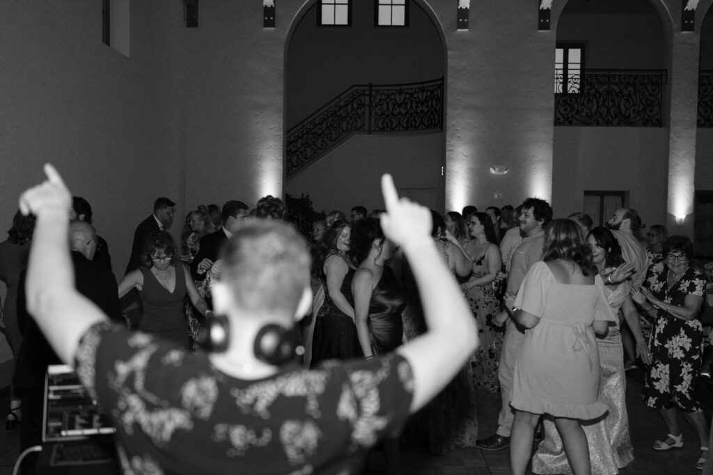 The DJ throws his hands in the air, guests dancing in the background.