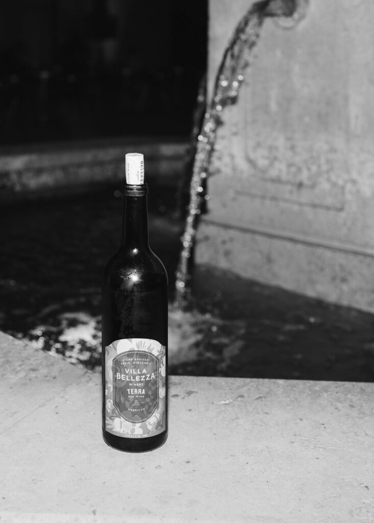 A close up of a bottle of Villa Bellezza wine on the edge of the courtyard fountain.